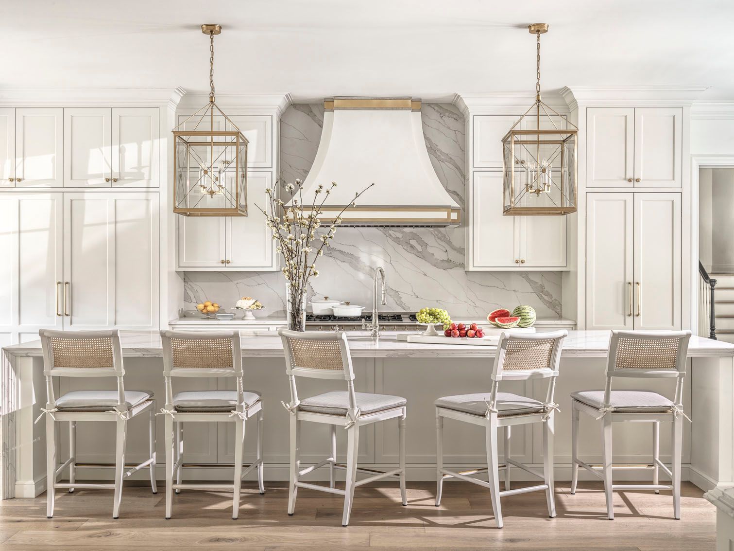 Elegant white kitchen with marble island, gold accents, and transparent bar stools
