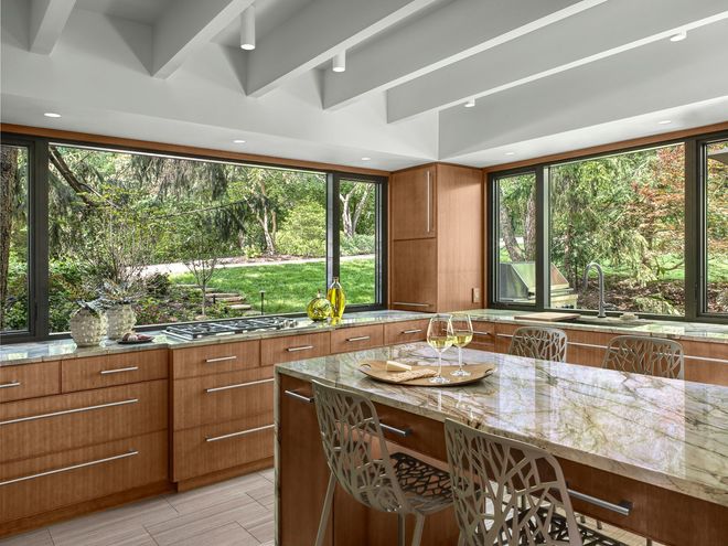 Modern kitchen with wood cabinets, granite island, and large windows overlooking a green wooded view