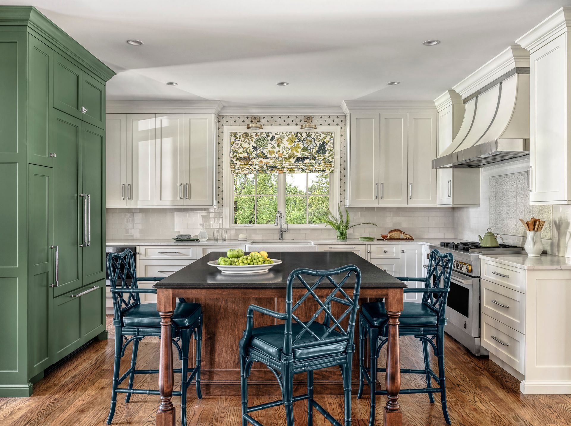 Bright kitchen with green cabinets, white island, and dark blue chairs around a wooden table