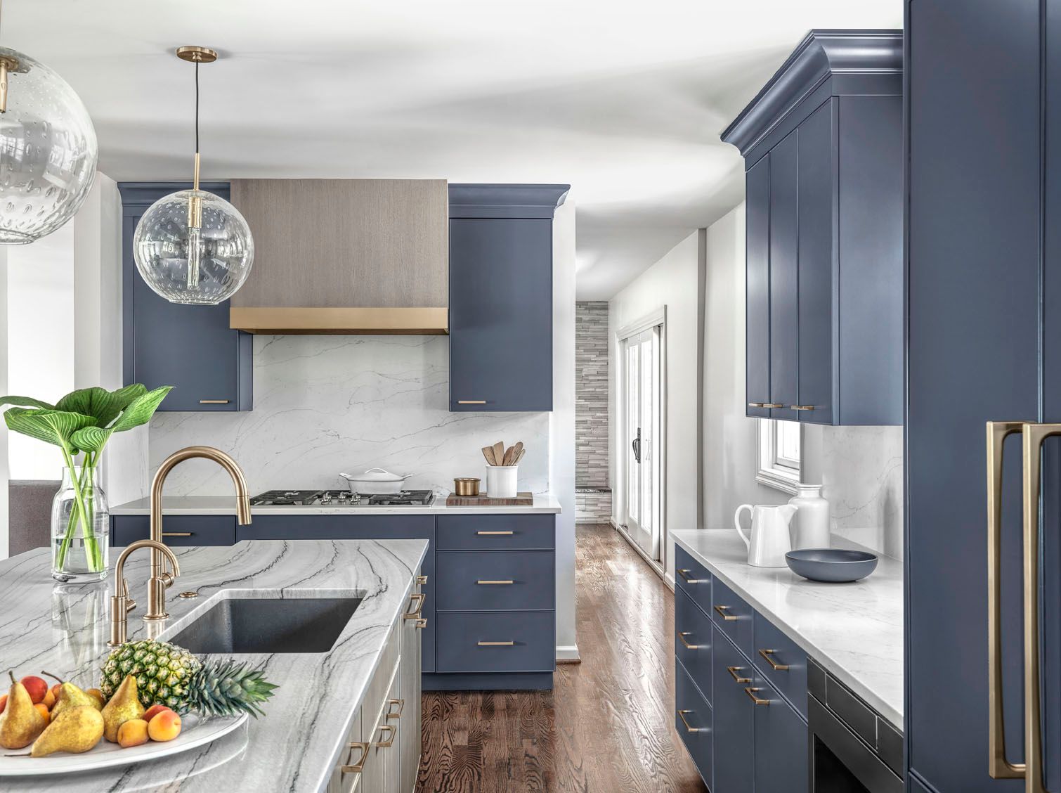Modern kitchen with blue cabinets, marble island, brass faucet, and pendant lights.