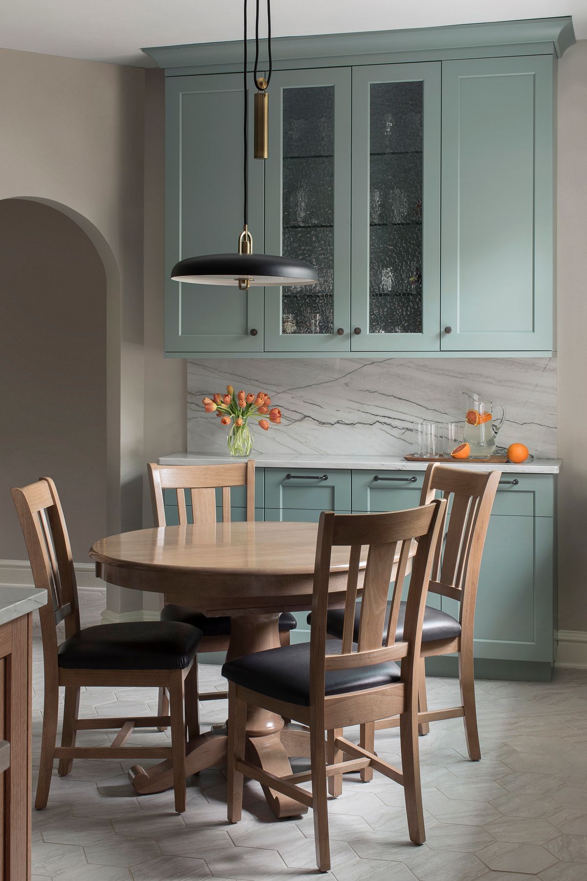 Dining nook with mint-green cabinets, round wooden table, and pendant light in a cozy kitchen.