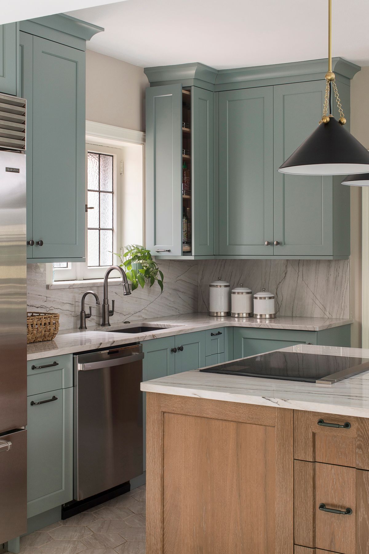 Modern kitchen with sage green cabinets, wood island, marble countertops, and black pendant light