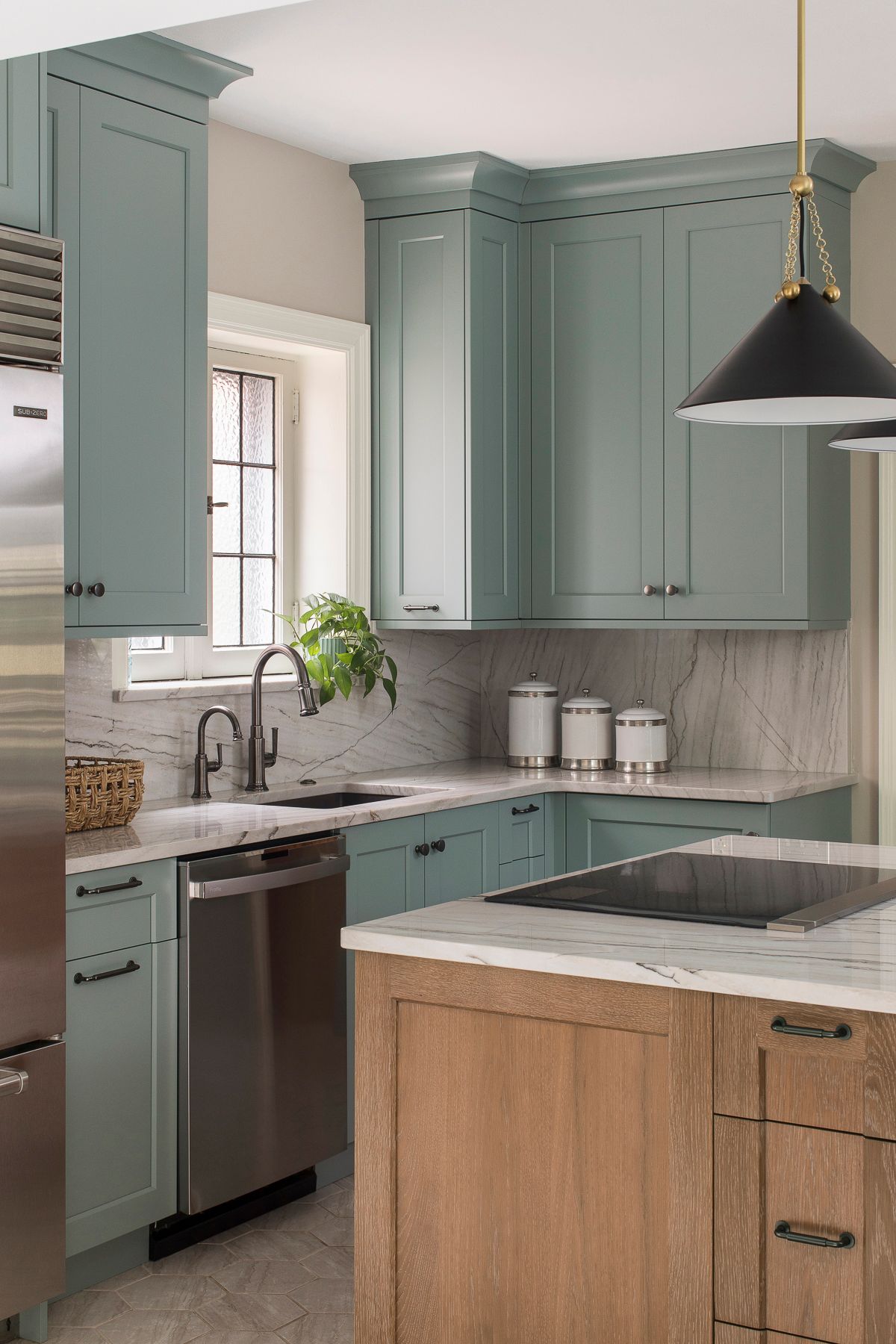 Modern kitchen with sage green cabinets, wood island, marble counters, and black pendant light