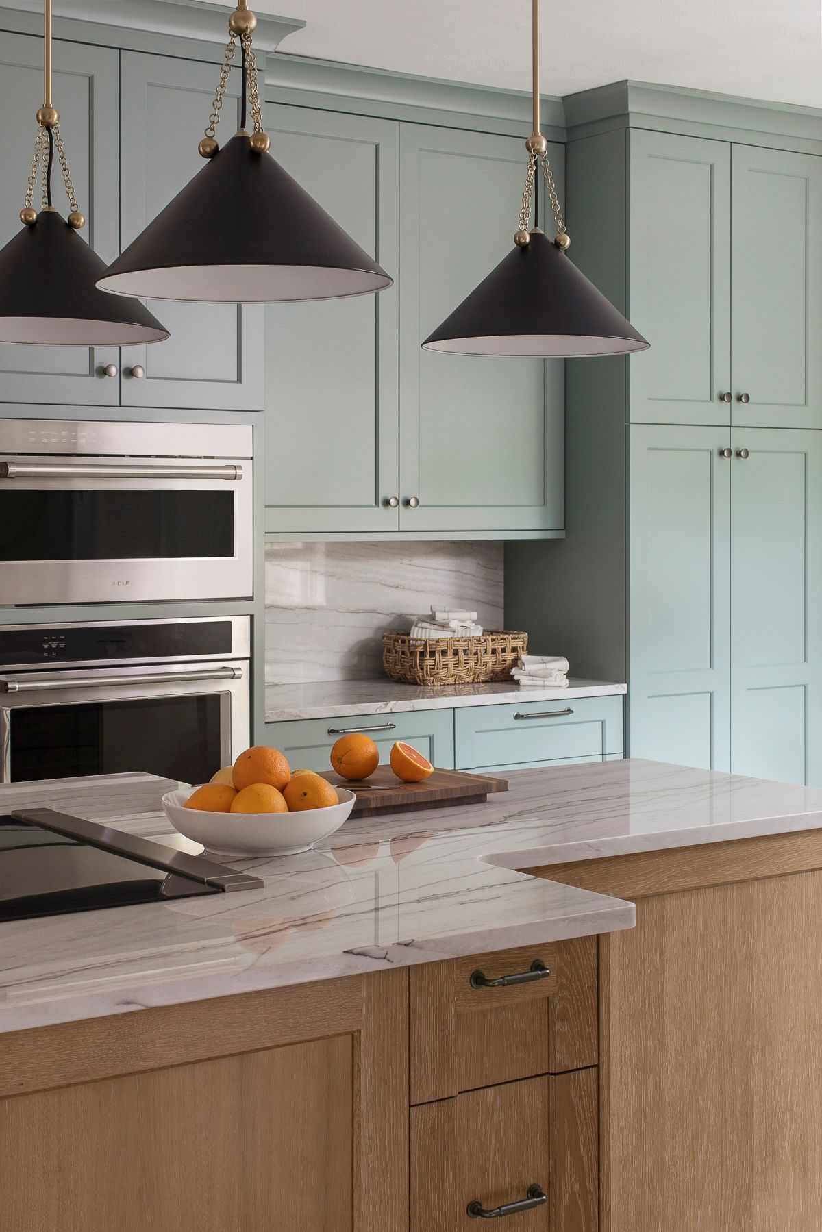 Modern kitchen with mint cabinets, black pendant lights, white countertop, and fruit bowl on the island