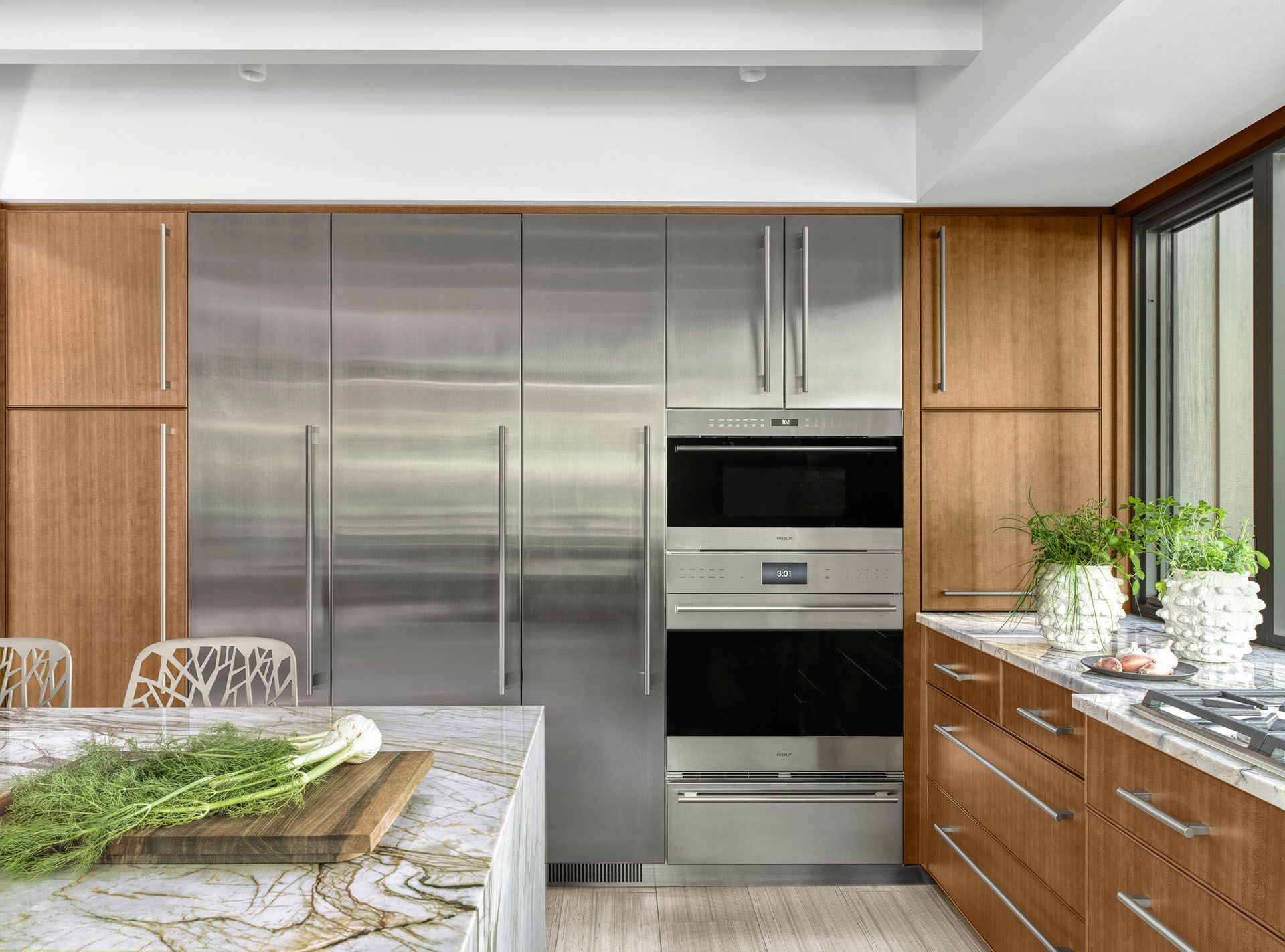 Modern kitchen with stainless steel appliances, wood cabinets, and a marble island under bright natural light