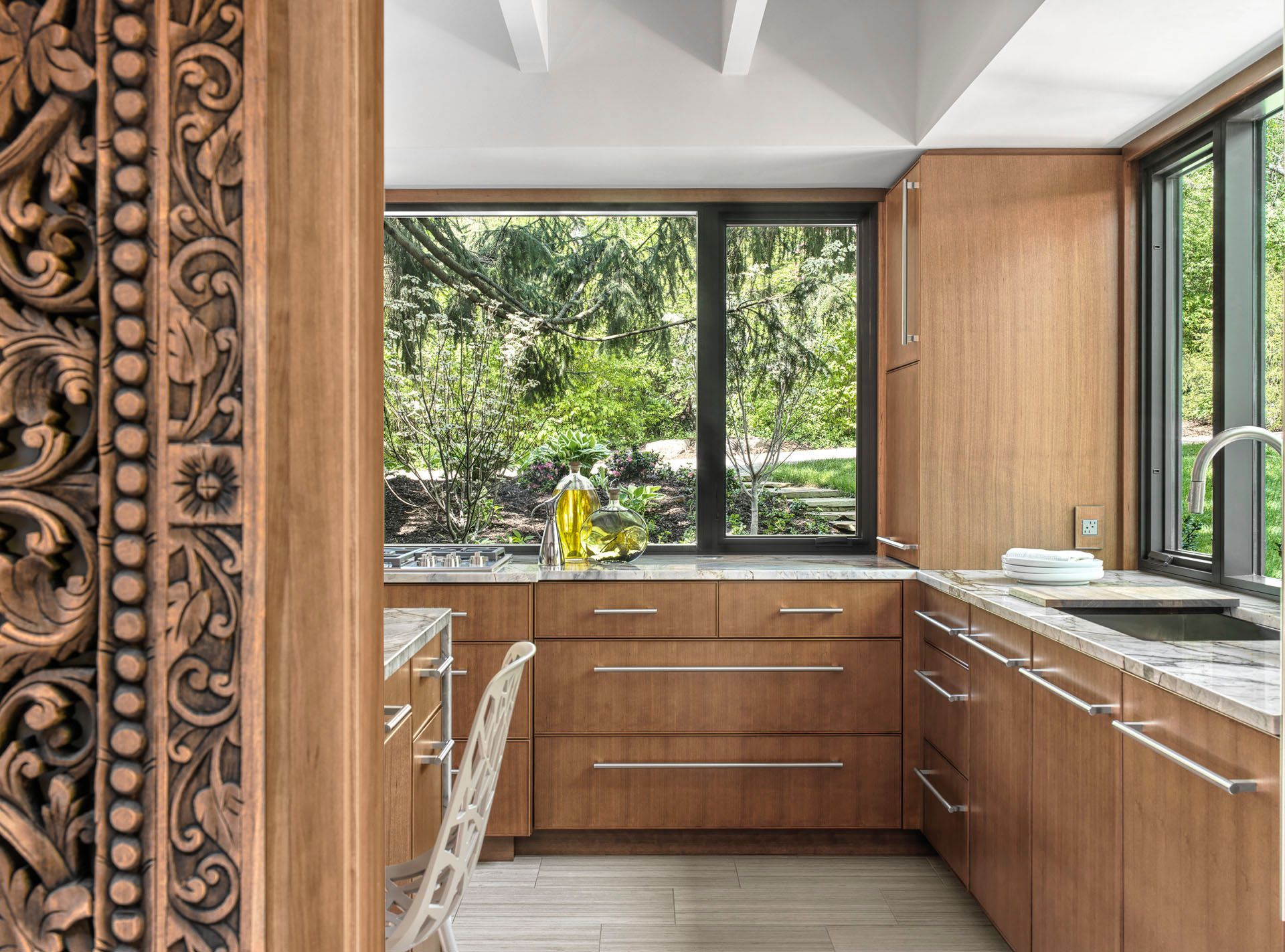 Modern kitchen with wood cabinets, stone counters, and large windows overlooking greenery