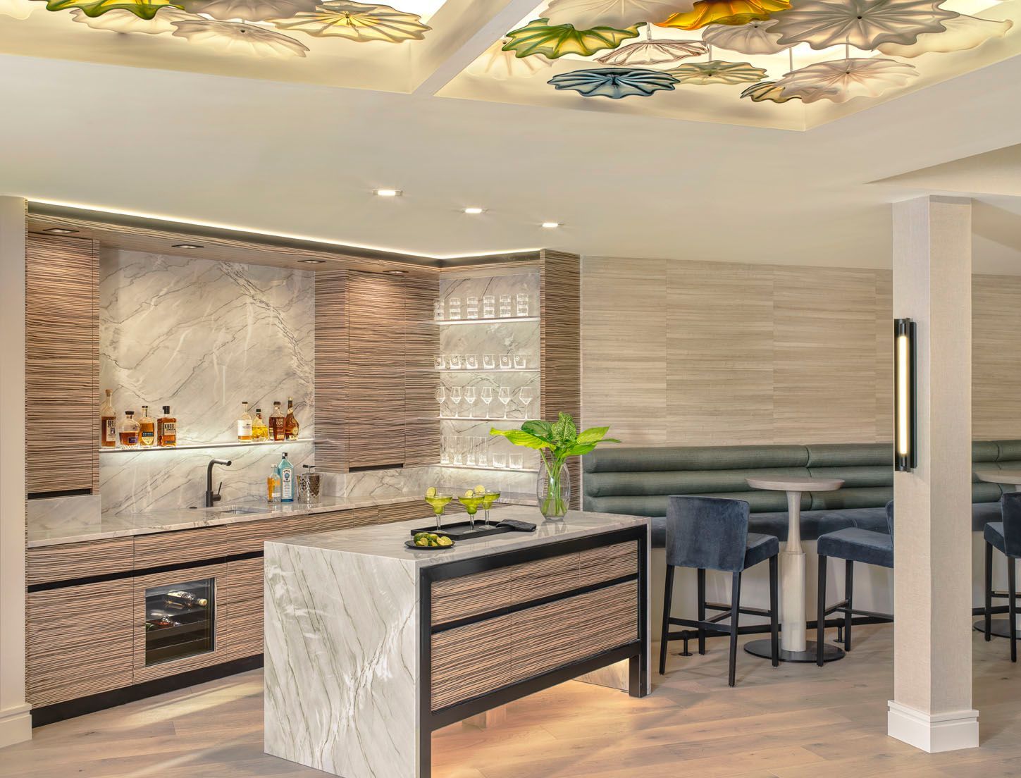 Modern kitchen with marble island, wood cabinetry, and a breakfast bar under decorative ceiling art.