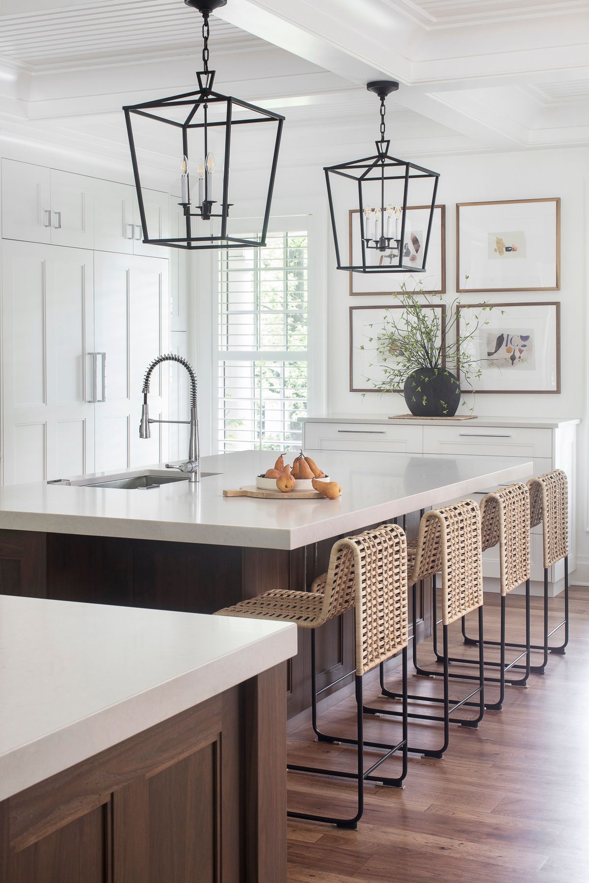 Modern white kitchen with marble island, woven barstools, and black pendant lights.
