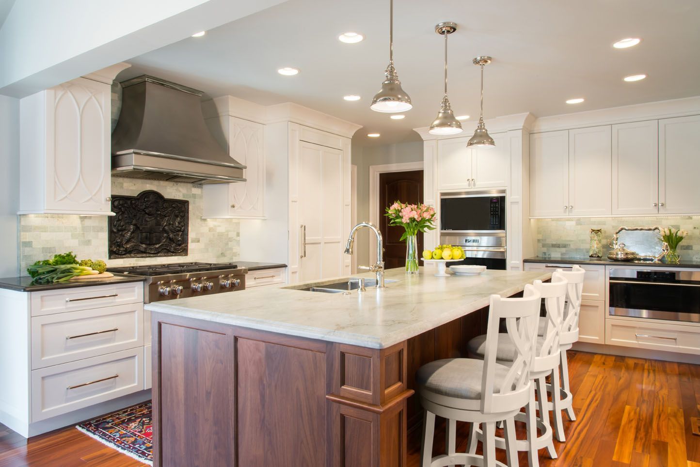 Bright white kitchen with large island, pendant lights, stainless range, and hardwood floors