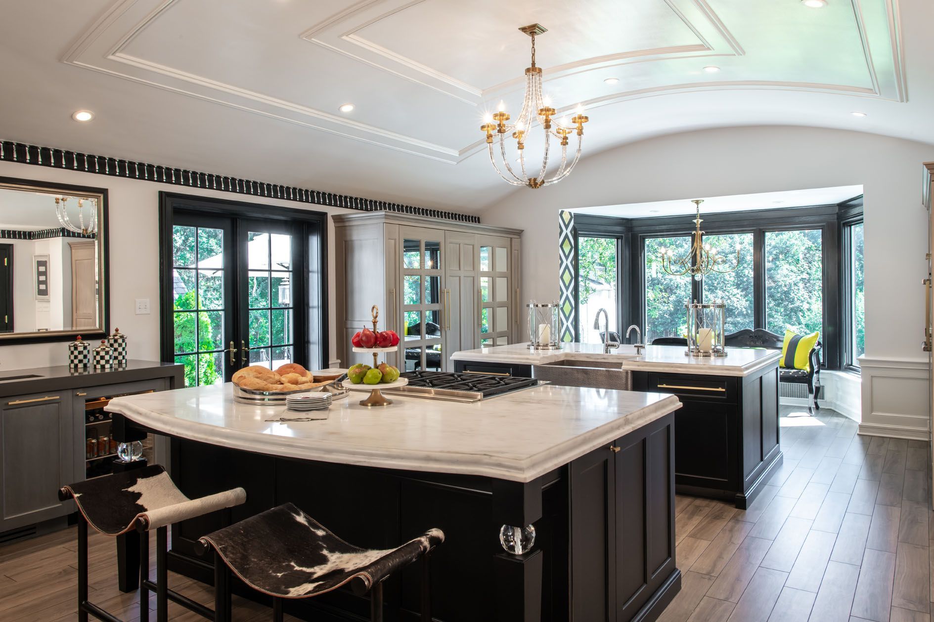 Bright modern kitchen with white marble island, dark cabinetry, and large windows overlooking greenery