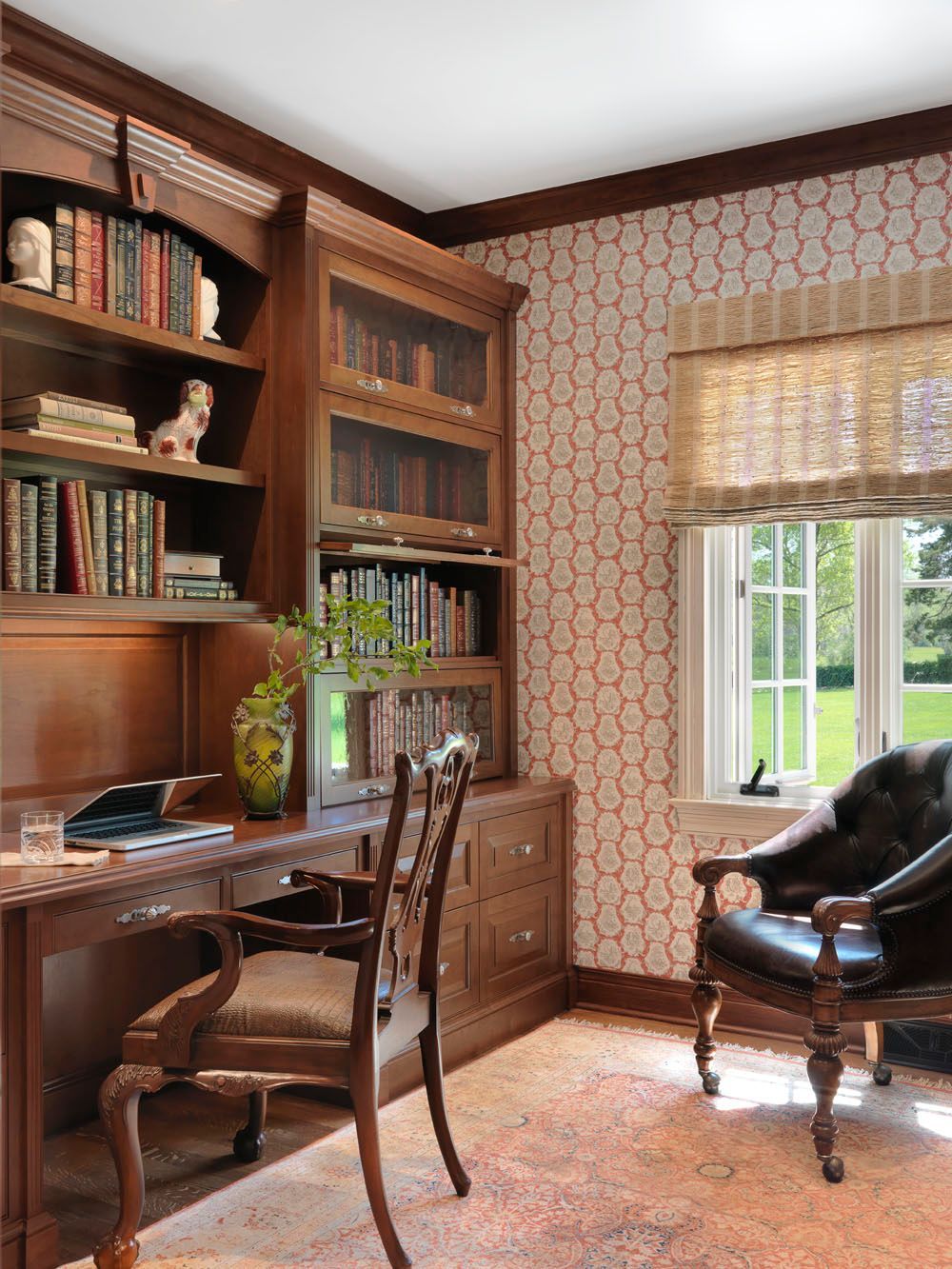 Cozy home office with wood bookshelves, a desk and chair, patterned wallpaper, and a window seat by a bright window