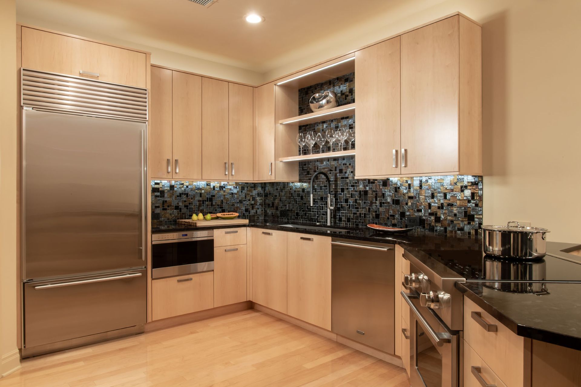 Modern kitchen with stainless steel fridge, light wood cabinets, black tile backsplash, and granite counters