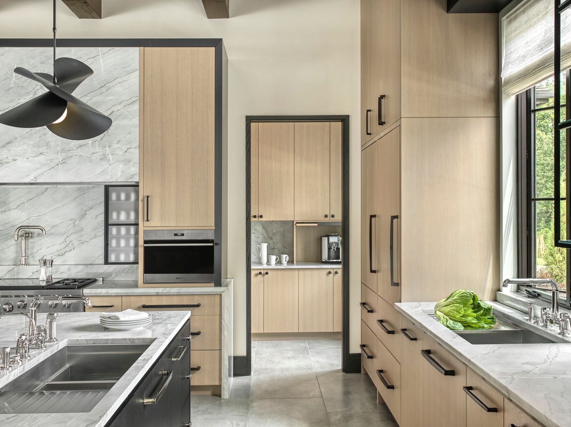 Modern kitchen with light wood cabinetry, gray island, built-in oven, and bright window over the sink.