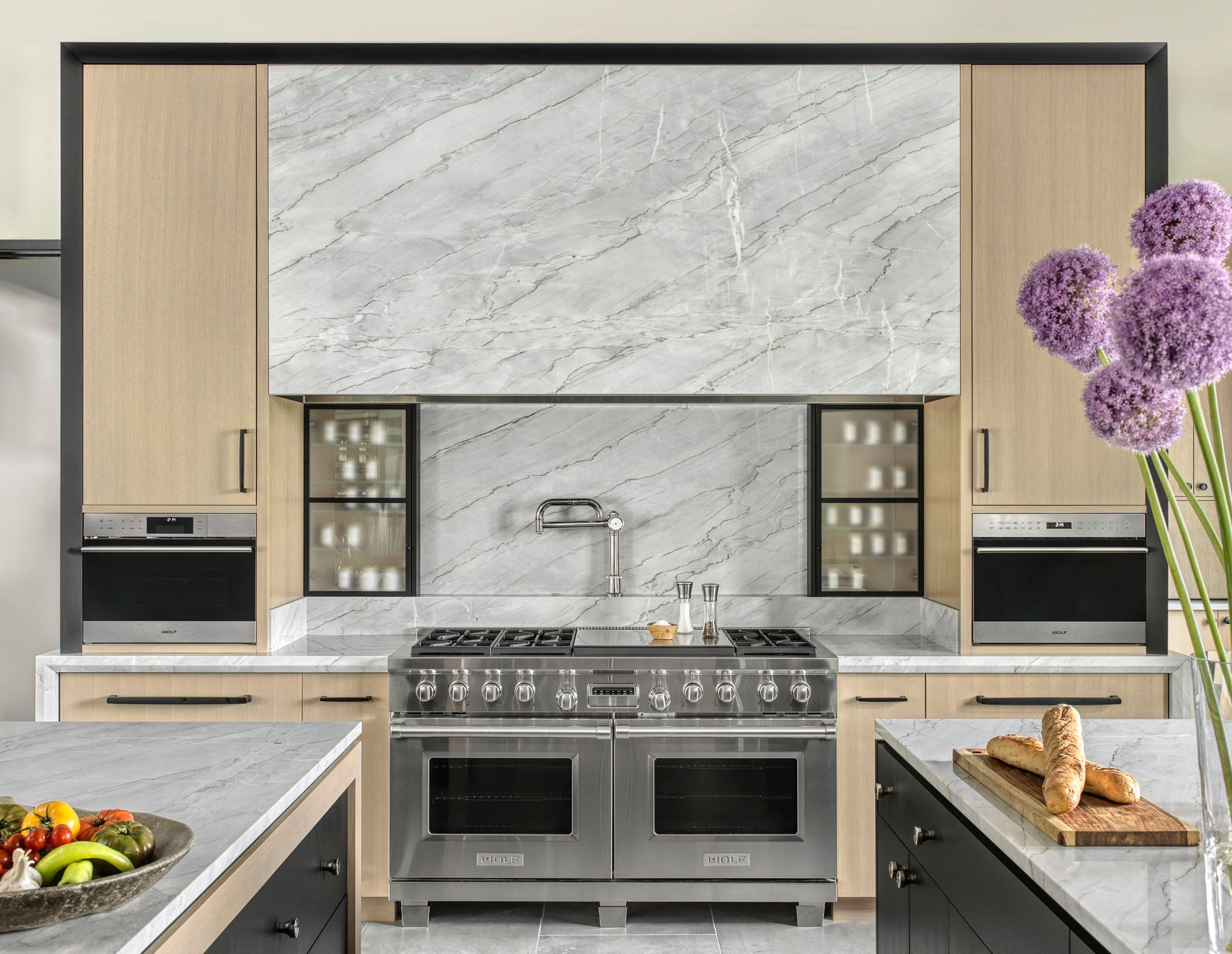 Modern kitchen with marble backsplash, stainless steel range, and light wood cabinets