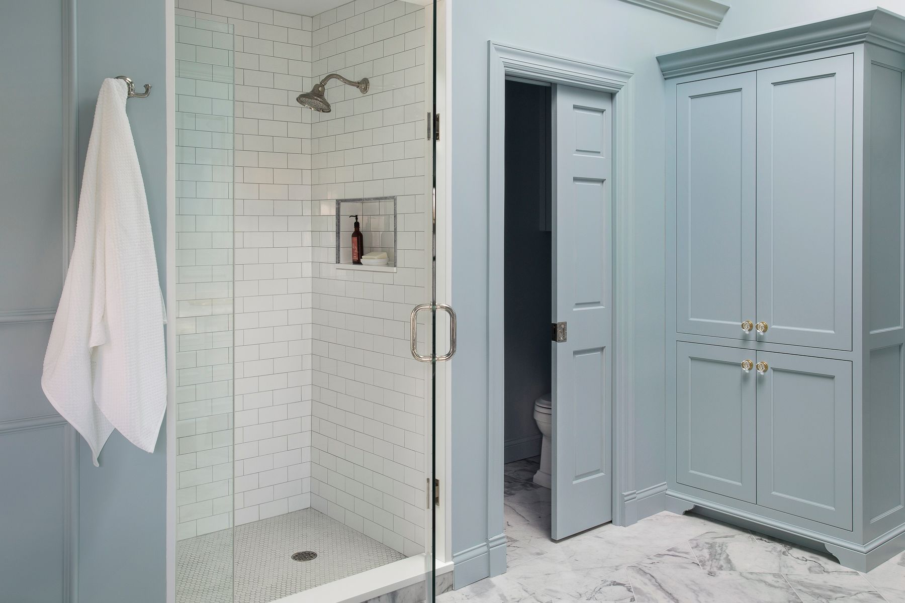 Modern bathroom with glass shower, white tile, blue cabinets, and a towel hanging on the wall
