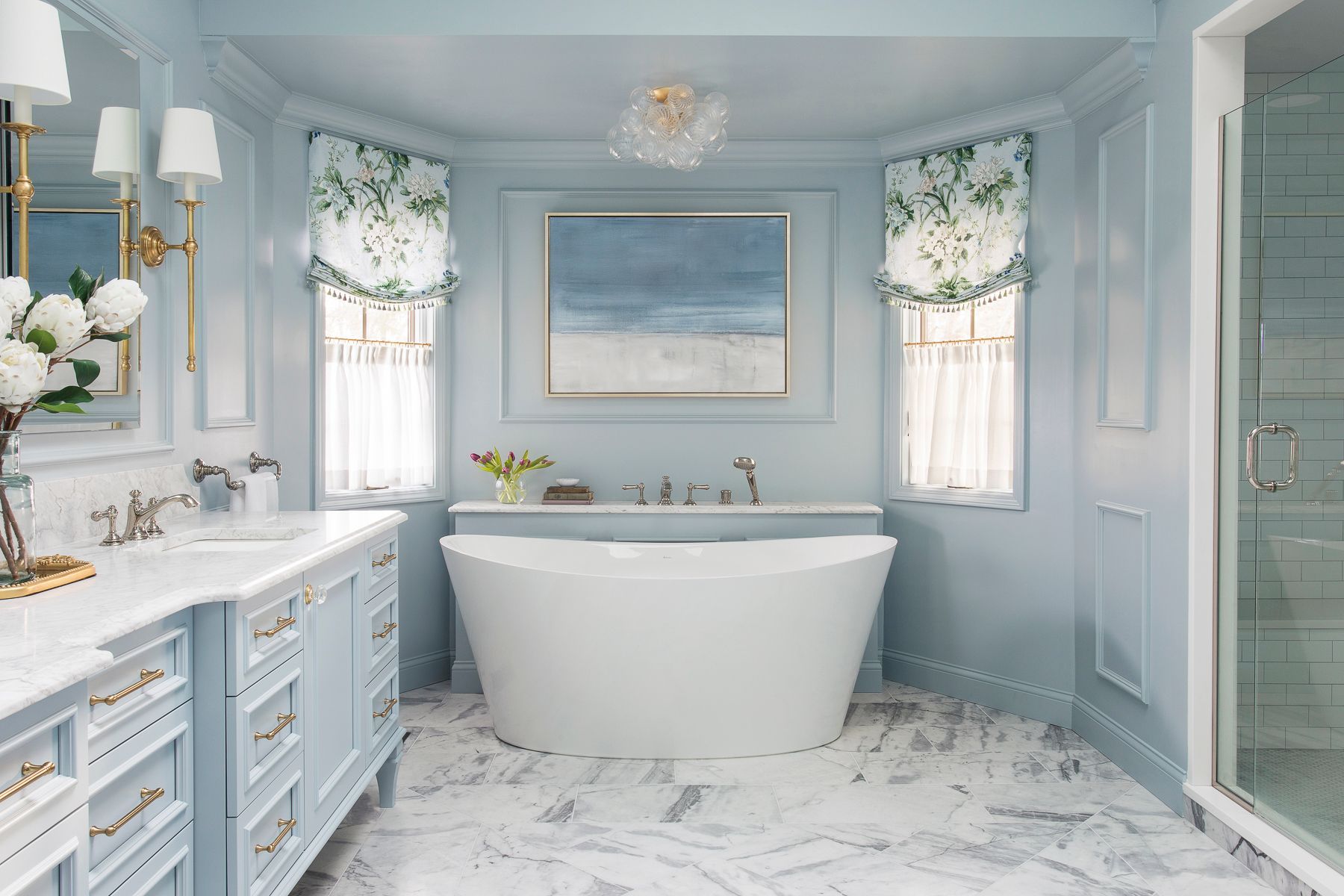 Bright pale-blue bathroom with freestanding tub, marble floor, double vanity, and glass shower enclosure