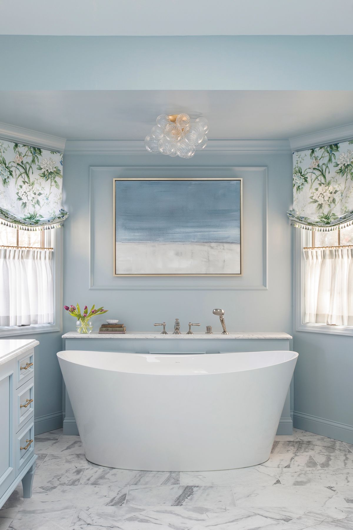 Bright blue bathroom with a freestanding tub, marble floor, and seascape painting above it