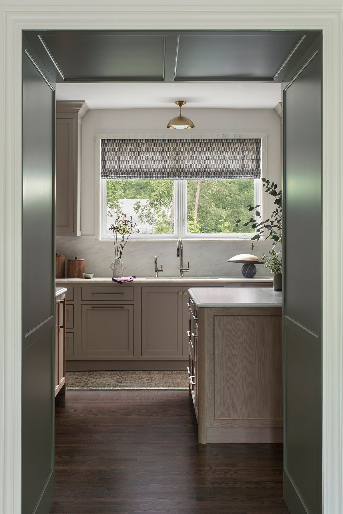 Small kitchen with light cabinetry, a window over the sink, and dark wood flooring viewed through a doorway