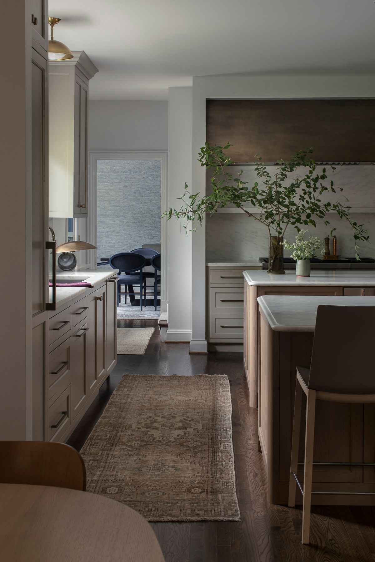 Modern kitchen with island, dining nook, and a rug leading to a bright hallway.