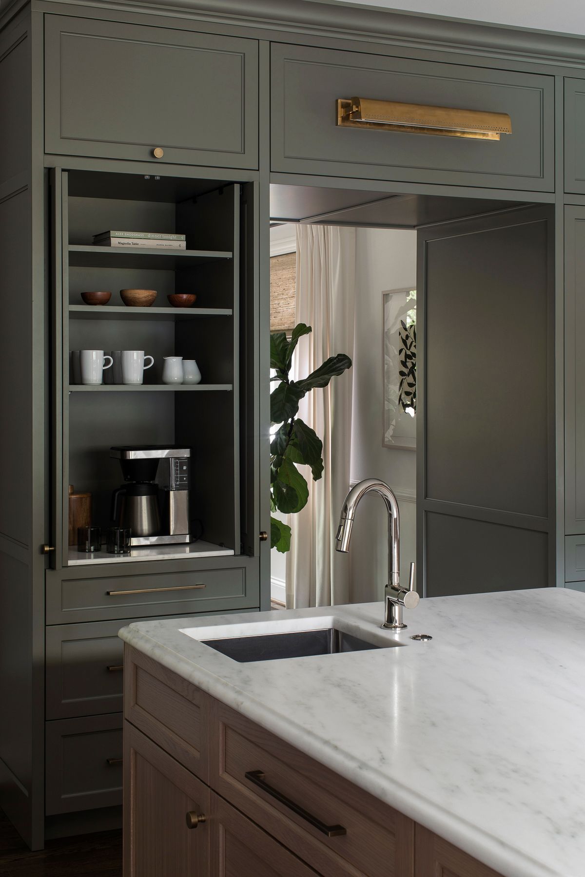 Modern kitchen with gray cabinets, open shelves, marble island, and sink under a large mirror or pass-through window