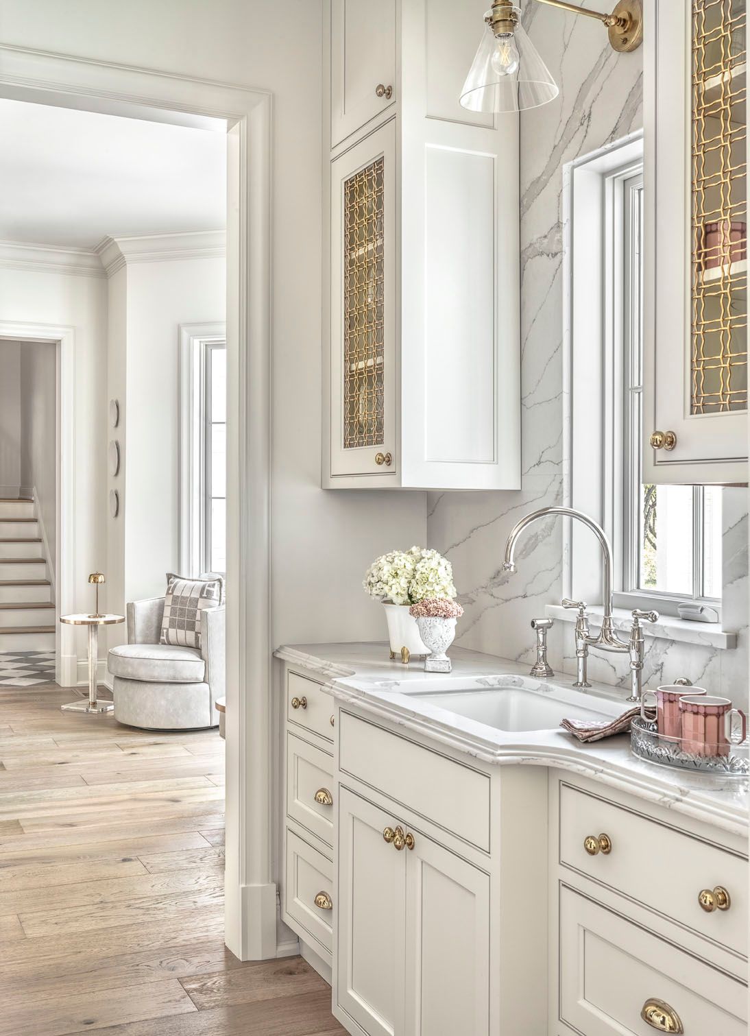Elegant white bathroom vanity with gold accents, marble countertop, sink, and a view into a bright bedroom