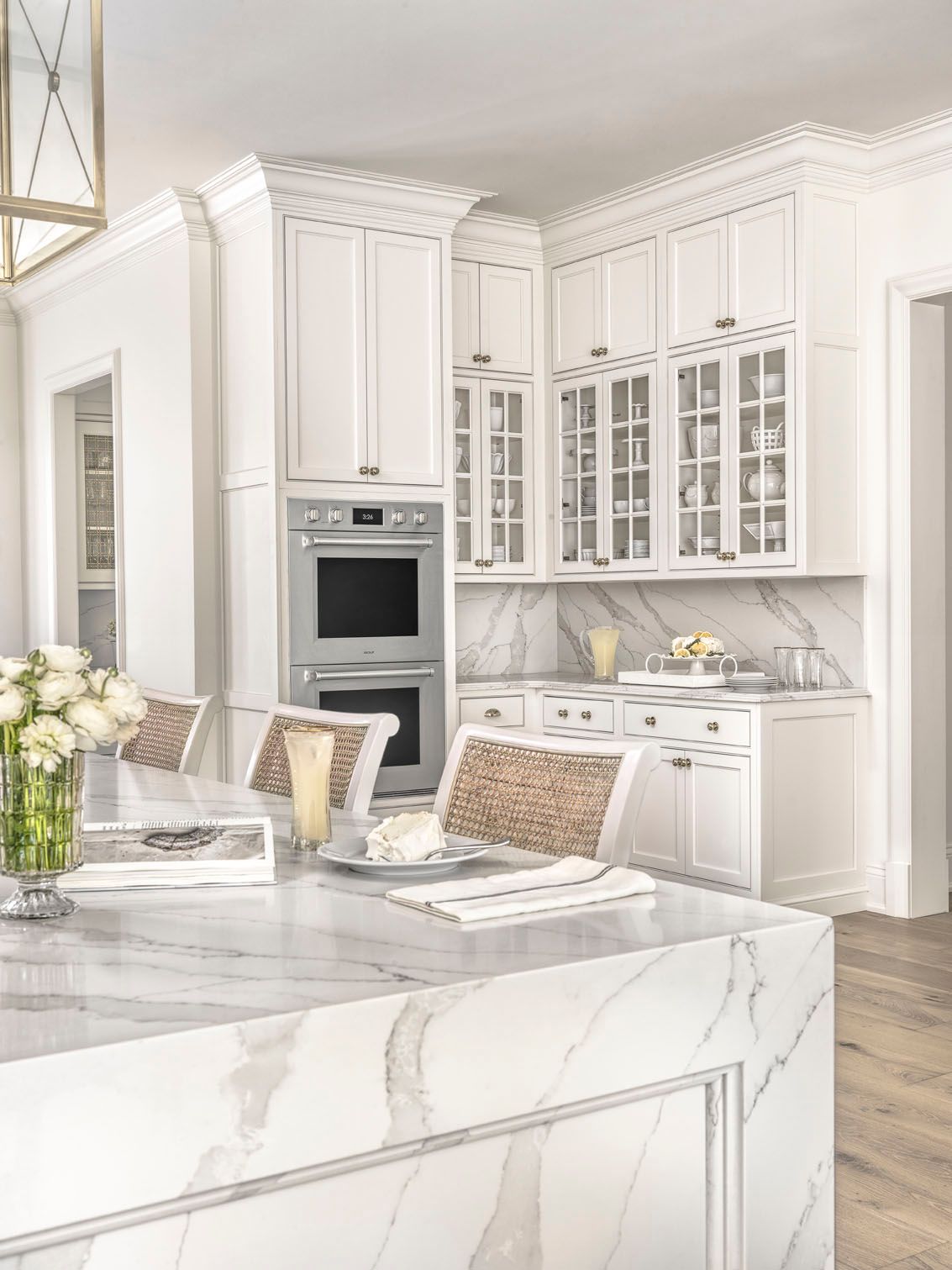 Bright white marble kitchen with glass-front cabinets and a large island