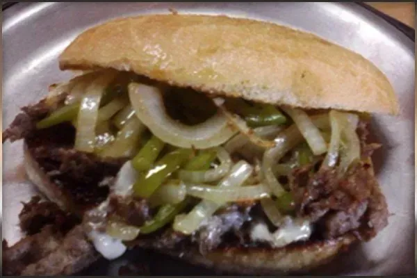 A close up of a sandwich with onions and peppers on a plate