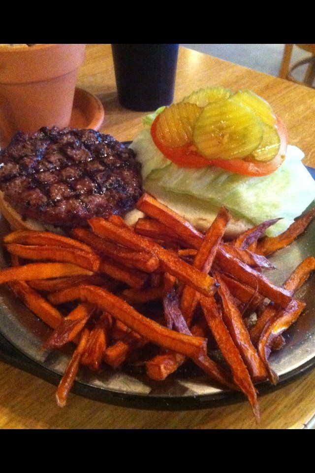A hamburger and sweet potato fries on a plate on a table.