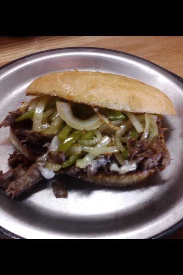 A steak sandwich with onions and green peppers on a plate.