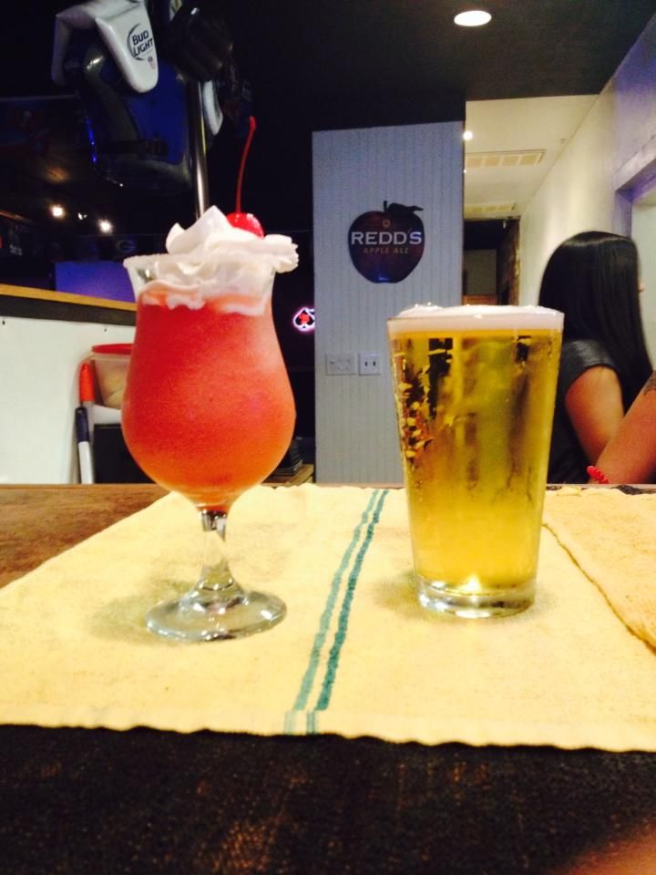 Two drinks on a table with a sign in the background that says redcorn