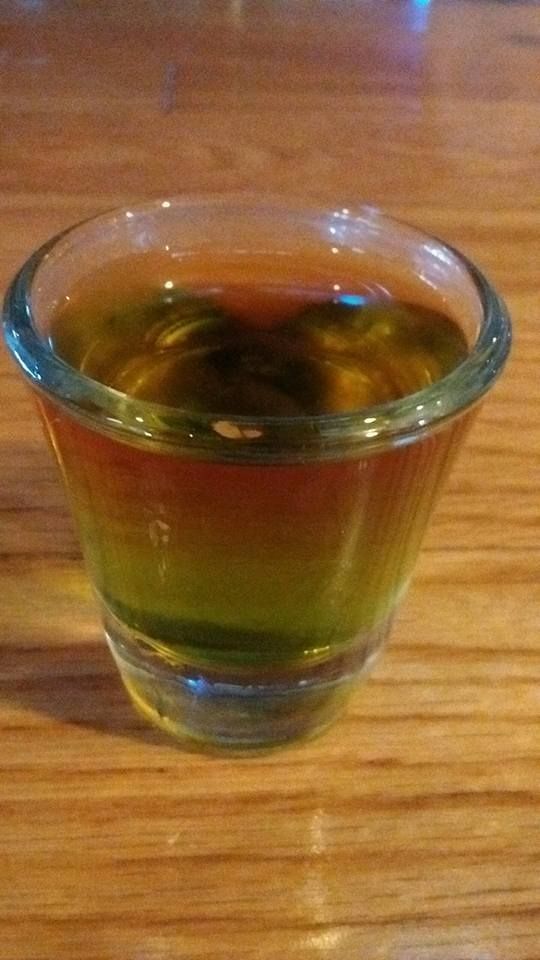 A shot glass filled with a green liquid is sitting on a wooden table.