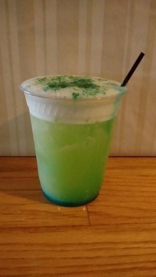 A green drink in a plastic cup with a straw on a wooden table.