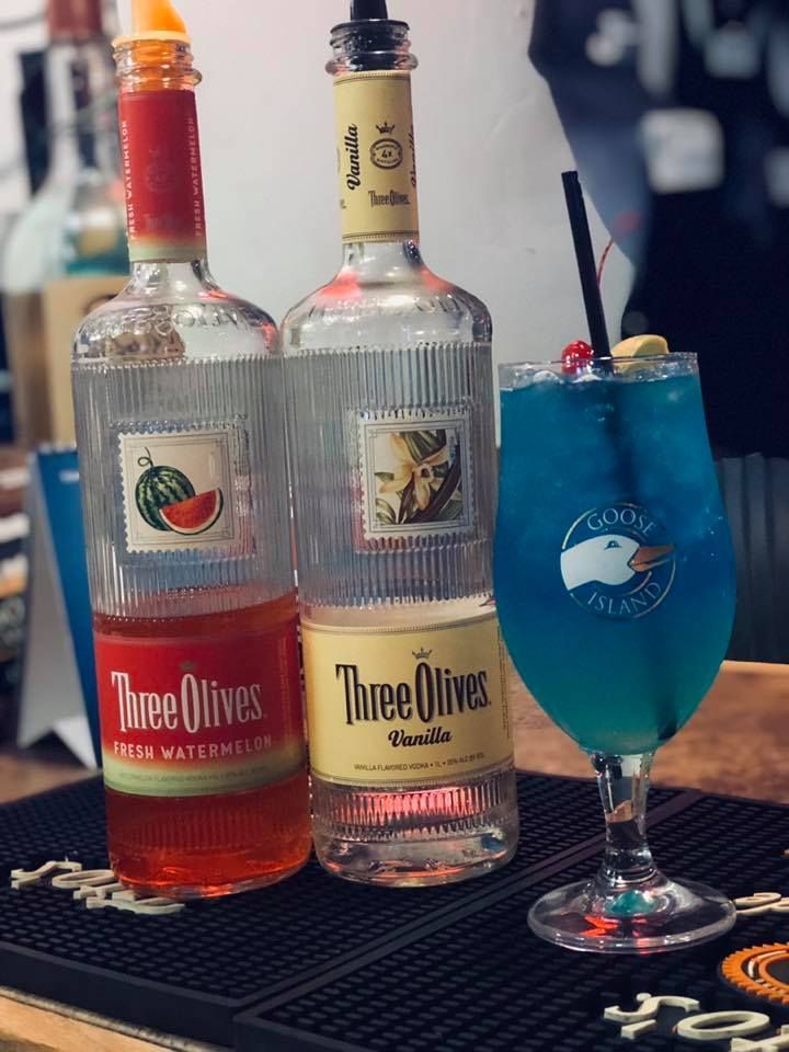 Two bottles of three olives and a glass of blue liquid