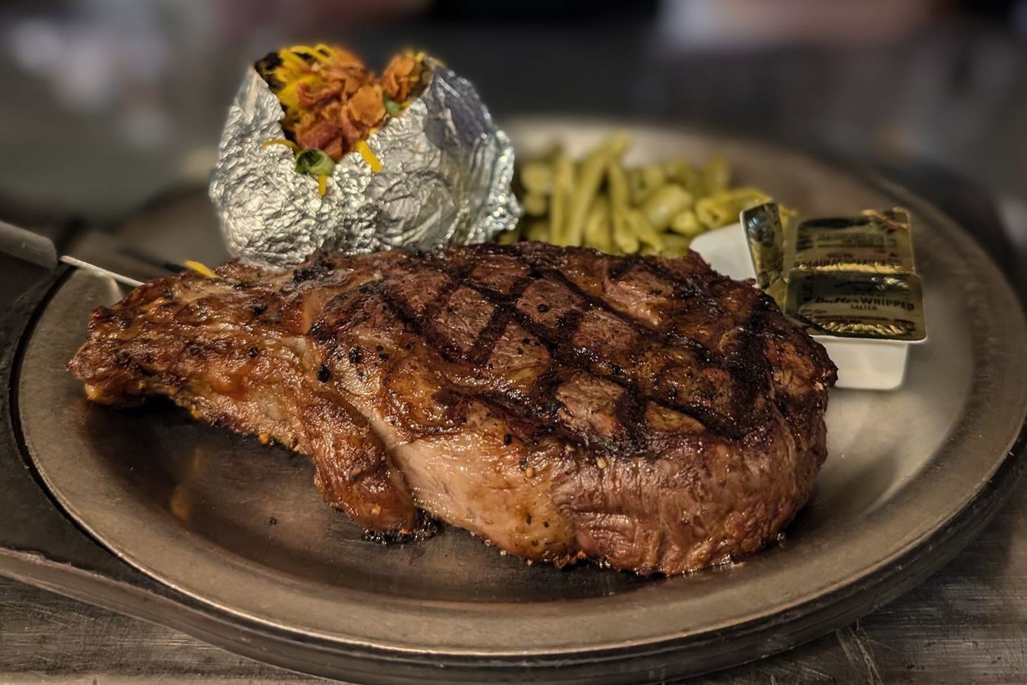 A steak with a baked potato and green beans on a plate.