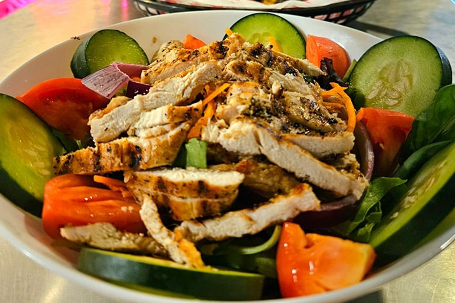 A salad with chicken , tomatoes , cucumbers and onions in a bowl on a table.