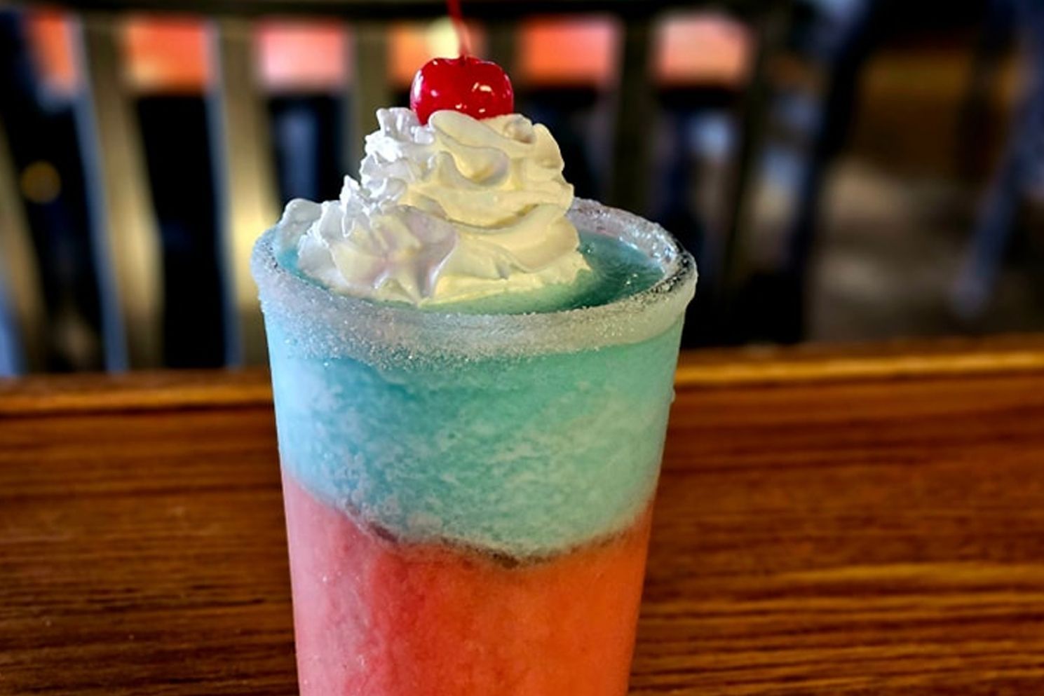 A red , white and blue drink with whipped cream and a cherry on top.