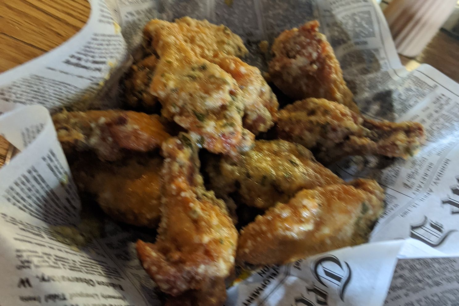 A basket of fried chicken wings is wrapped in newspaper