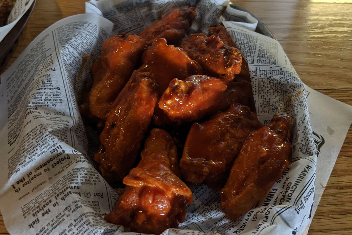 A basket of chicken wings wrapped in newspaper on a table