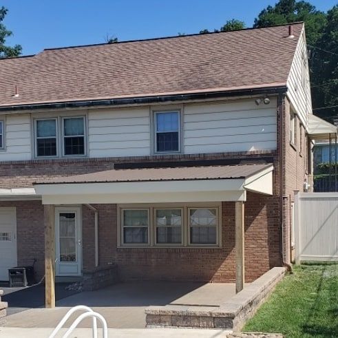 Two-story brick building with brown roof and covered porch. Beige siding and multiple windows visible.