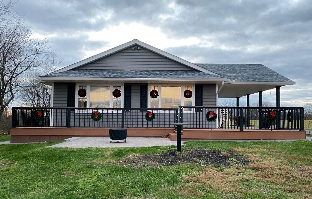 Gray house with black railing porch, decorated with Christmas wreaths. Cloudy sky.