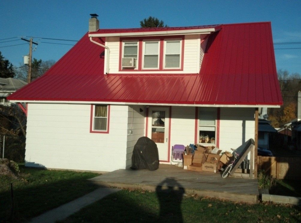 White house with red metal roof; boxes and items on the porch.