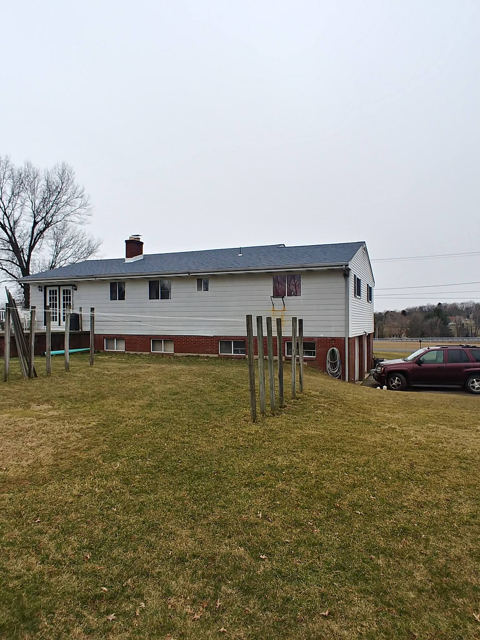 White house with red brick foundation, brown grass field, fence in front, and a maroon truck.