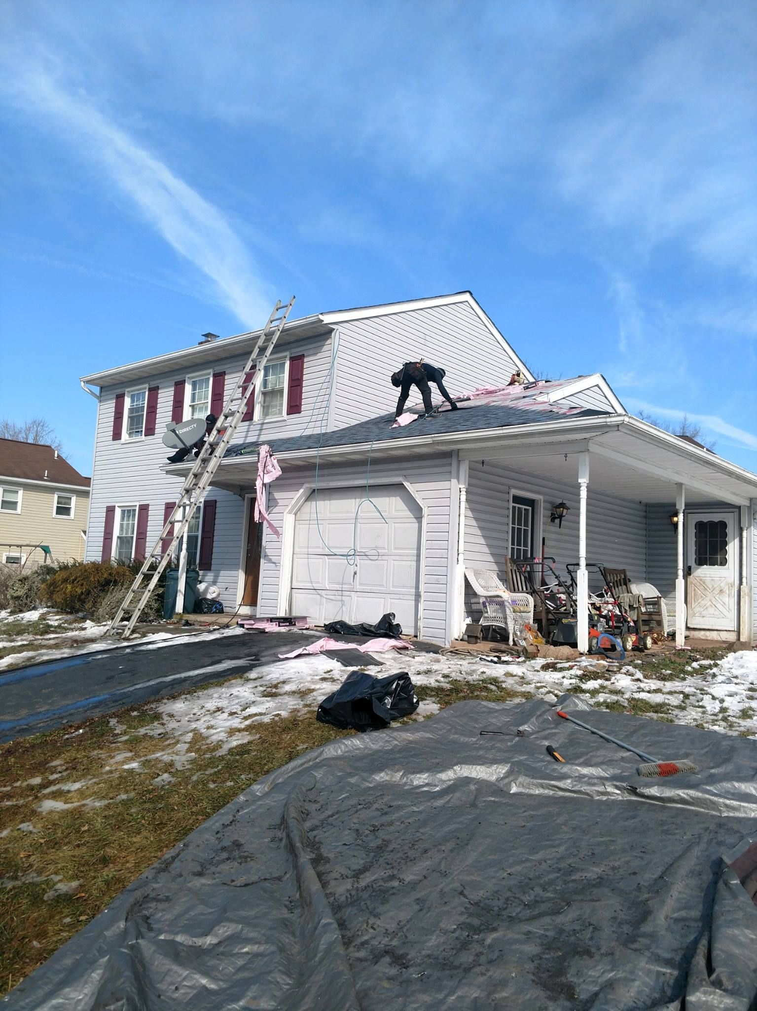 House with workers on roof; ladder against side, blue sky.