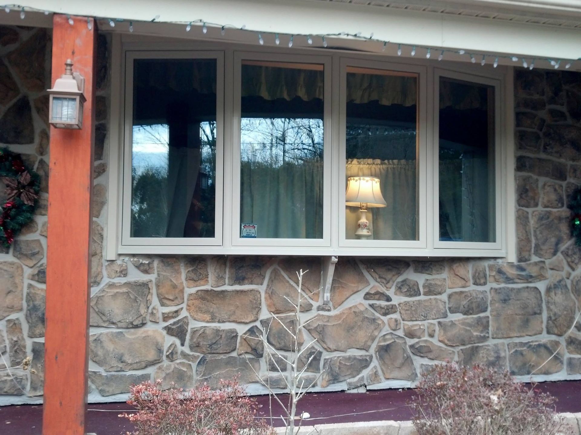 Bay window with beige frames, set in a stone exterior, reflecting a lit lamp.