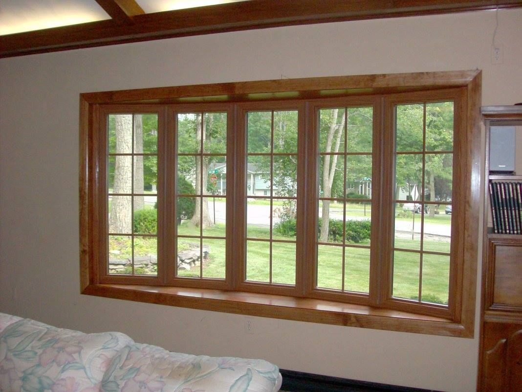 Bay window with wooden frame, overlooking a green yard and trees.