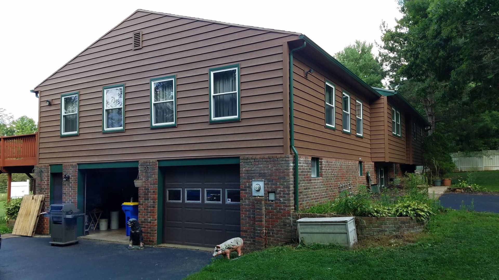 Brown house with two garage doors, windows, and a dog on the lawn.