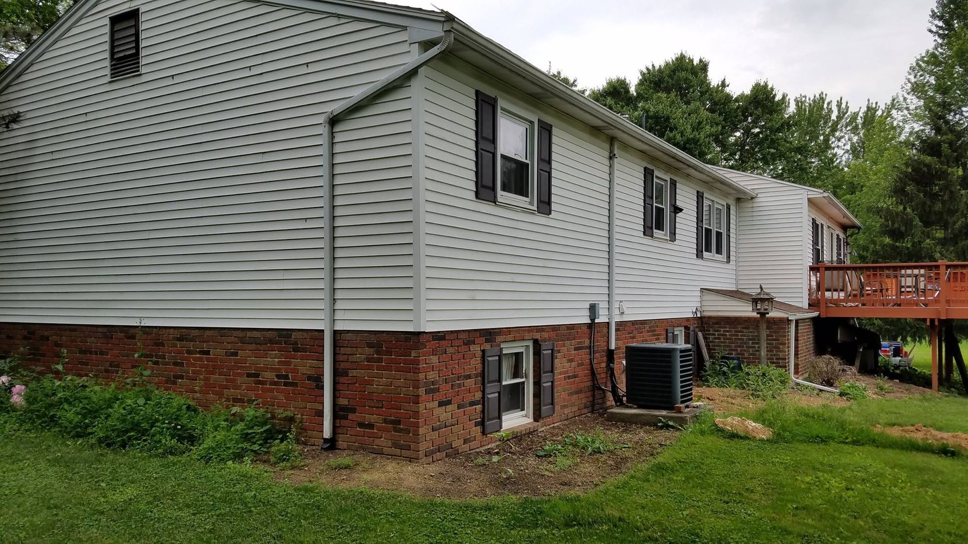 Two-story house with white siding over a brick base, black shutters, and a wooden deck.