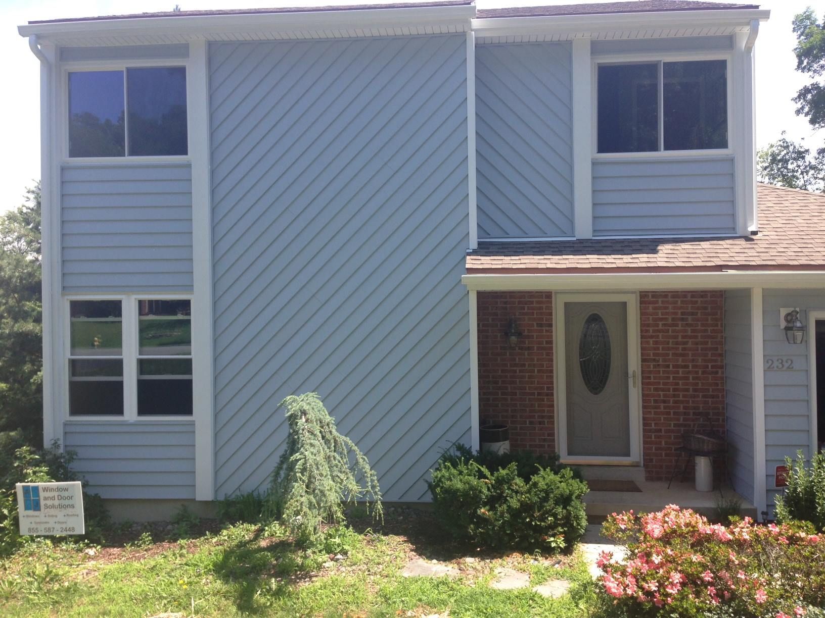 Two-story house with light blue siding. Angled siding on central section, brick entryway, and brown roof.