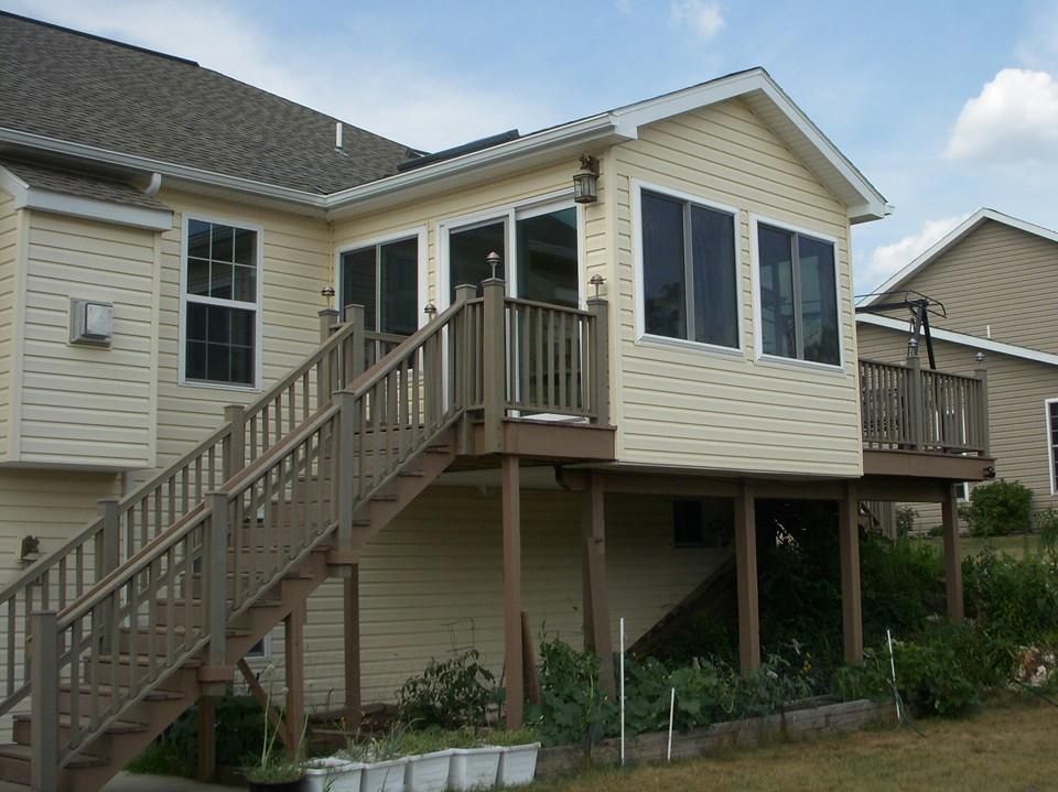 Tan house with a deck and steps, surrounded by a lawn and garden.
