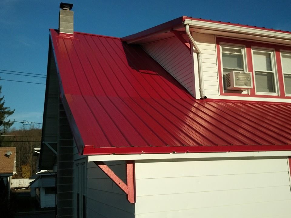 Red metal roof on a white house, with a chimney and windows, against a blue sky.